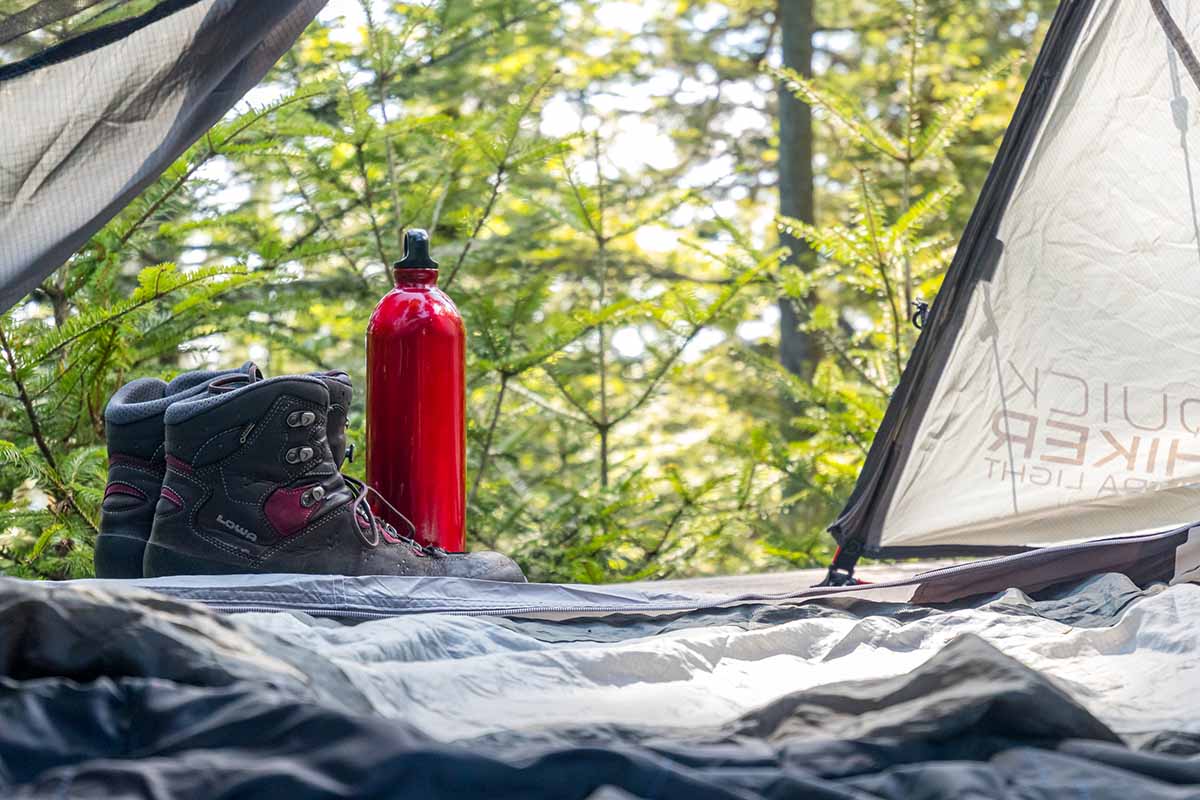 Blick aus dem Zelt auf eine Wasserflasche und Campingkocher